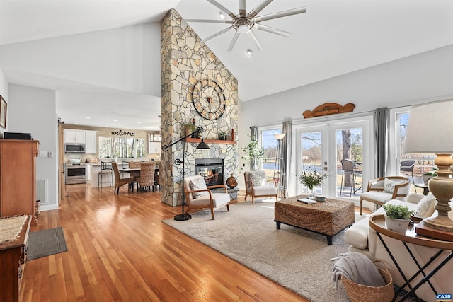 living area featuring visible vents, ceiling fan, light wood-type flooring, a fireplace, and high vaulted ceiling