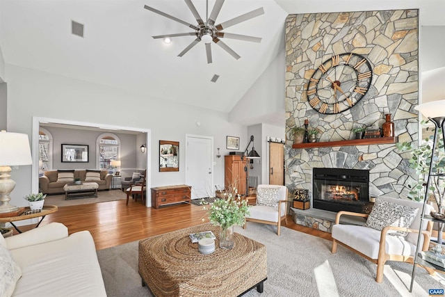 living room featuring wood finished floors, a ceiling fan, visible vents, high vaulted ceiling, and a fireplace