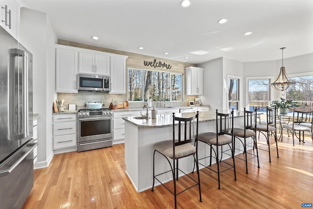 kitchen with light wood-style flooring, white cabinets, tasteful backsplash, and appliances with stainless steel finishes