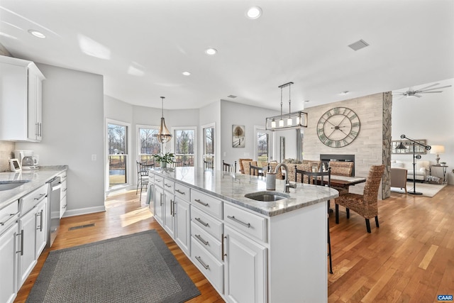 kitchen featuring light wood finished floors, an island with sink, a sink, white cabinets, and stainless steel dishwasher