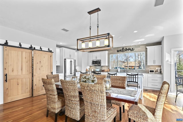 dining room featuring recessed lighting, light wood-type flooring, a barn door, and visible vents