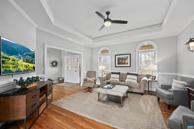 living area featuring ornamental molding, a ceiling fan, a tray ceiling, wood finished floors, and baseboards