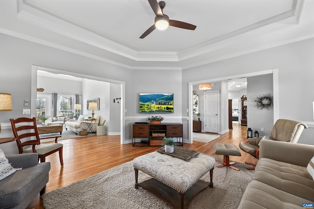 living area featuring light wood finished floors, a ceiling fan, a tray ceiling, and ornamental molding