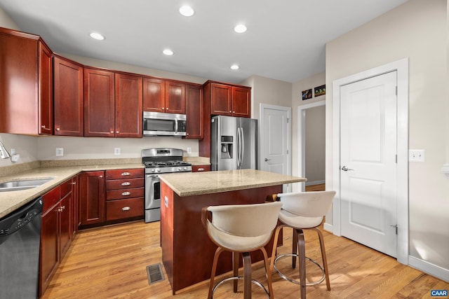 kitchen with visible vents, a kitchen island, stainless steel appliances, dark brown cabinets, and light wood-type flooring