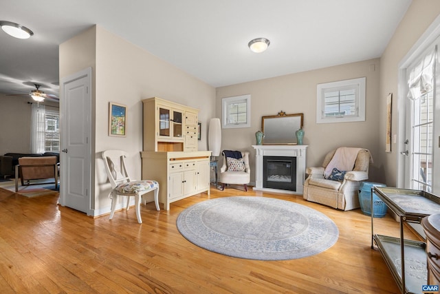 sitting room featuring a glass covered fireplace, plenty of natural light, baseboards, and light wood finished floors