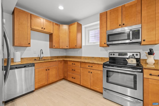 kitchen featuring a sink, recessed lighting, stainless steel appliances, brown cabinetry, and light stone countertops