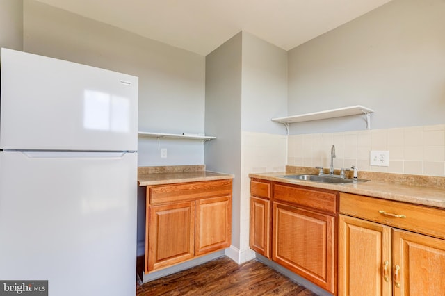 kitchen featuring dark wood-style floors, open shelves, freestanding refrigerator, a sink, and brown cabinets