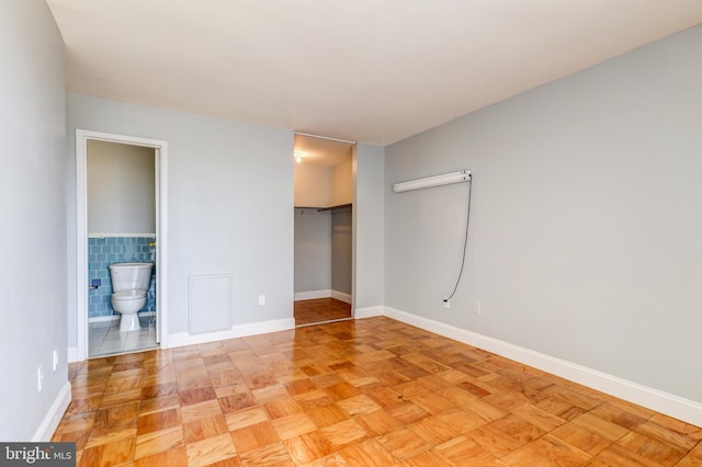 unfurnished bedroom with a walk in closet, baseboards, ensuite bathroom, a closet, and tile walls