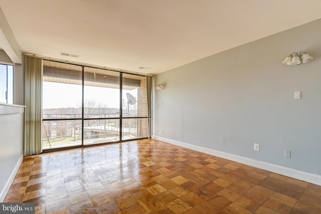 empty room with a wall of windows, visible vents, and baseboards