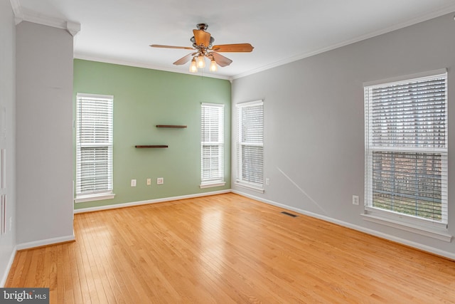 empty room featuring visible vents, ornamental molding, a ceiling fan, hardwood / wood-style floors, and baseboards