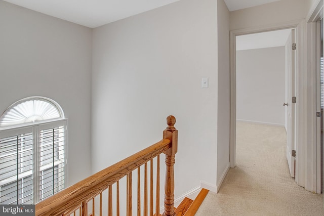 hallway featuring an upstairs landing, light colored carpet, and baseboards