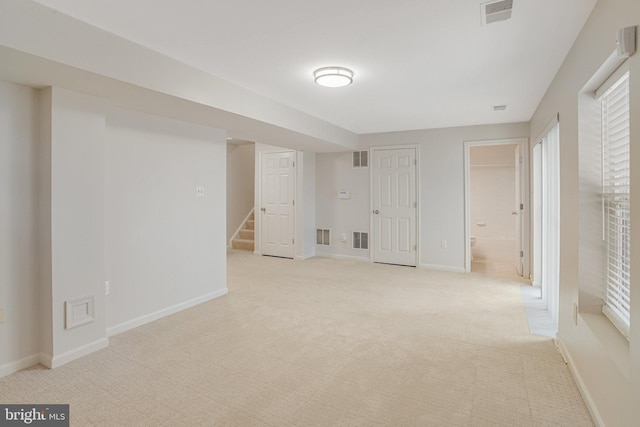 finished below grade area featuring visible vents, baseboards, light carpet, and stairway