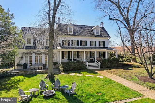 view of front of house featuring a front lawn, a fire pit, covered porch, and a chimney