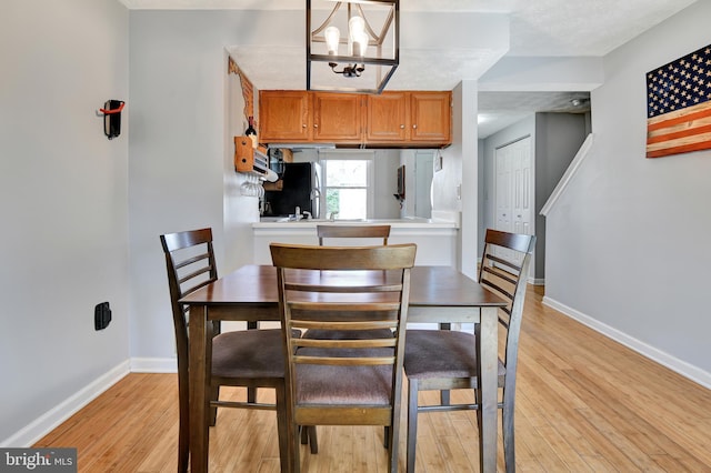 dining room with baseboards, a notable chandelier, and light wood finished floors