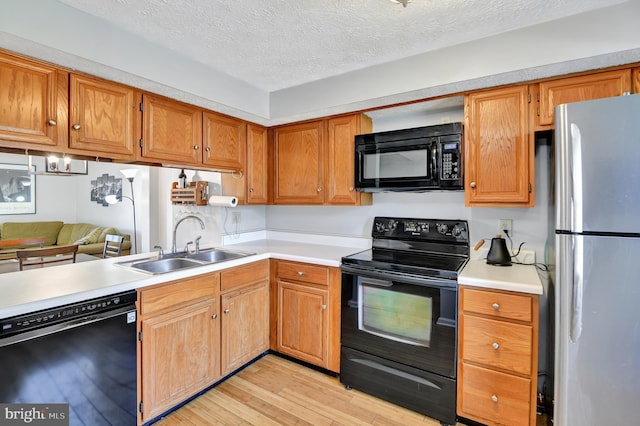 kitchen with a sink, black appliances, light countertops, light wood-style floors, and a textured ceiling