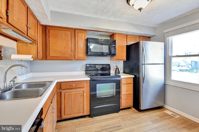 kitchen with light wood finished floors, visible vents, light countertops, black appliances, and a sink