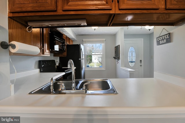 kitchen with a sink, black appliances, brown cabinetry, and light countertops