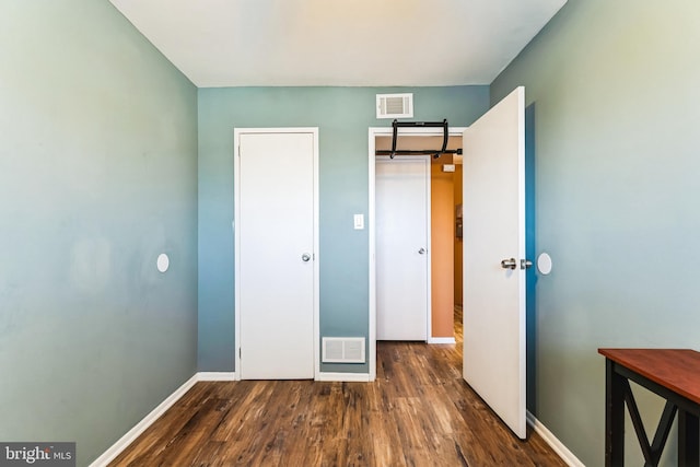 unfurnished bedroom featuring dark wood-style floors, visible vents, and baseboards