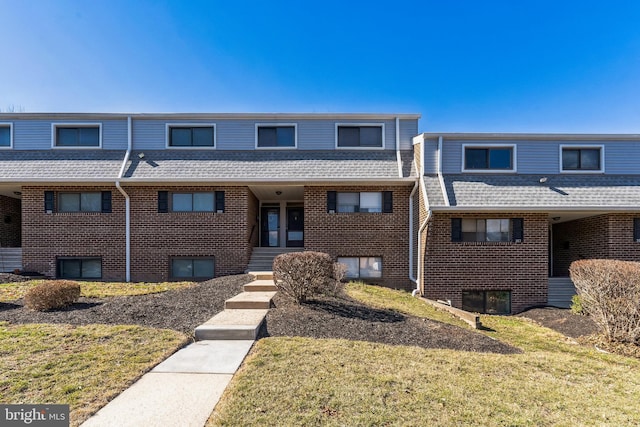 view of property with a front yard, brick siding, and roof with shingles