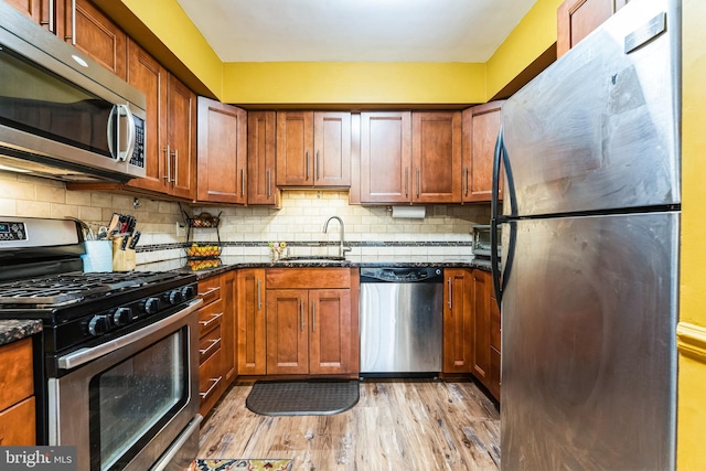 kitchen featuring dark stone counters, a sink, light wood-style floors, appliances with stainless steel finishes, and tasteful backsplash