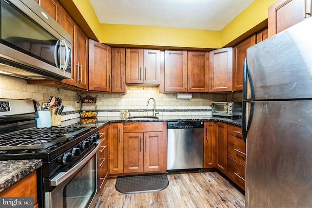 kitchen with decorative backsplash, dark stone countertops, light wood-style flooring, stainless steel appliances, and a sink