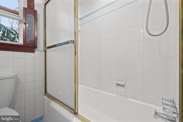 bathroom with tile walls, toilet, and bath / shower combo with glass door