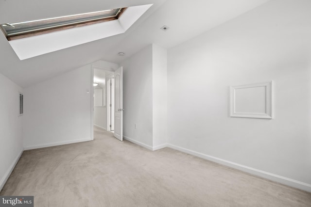 carpeted spare room with baseboards, vaulted ceiling with skylight, and visible vents