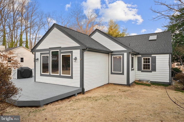 back of property with a lawn, a shingled roof, and a deck