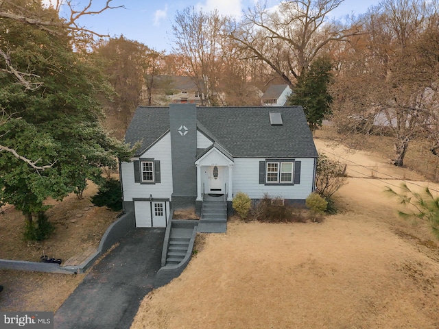 view of front of house with an attached garage, a chimney, driveway, and roof with shingles