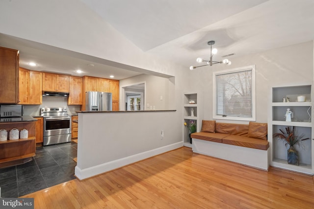 kitchen featuring under cabinet range hood, built in features, dark countertops, dark wood-style floors, and stainless steel appliances