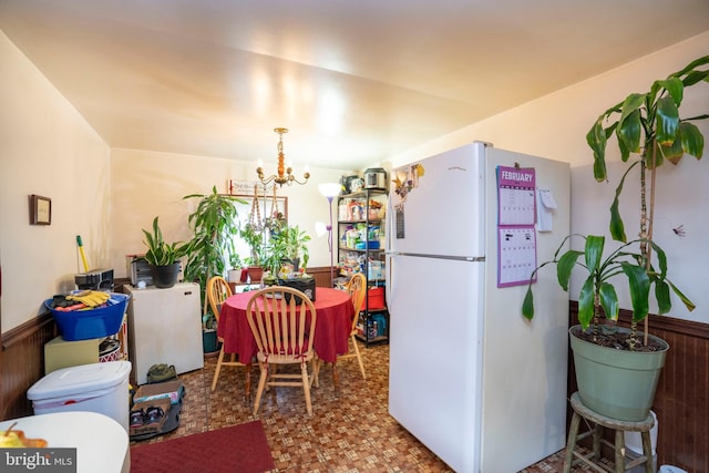 kitchen featuring a wainscoted wall, an inviting chandelier, wood walls, and freestanding refrigerator