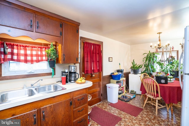 kitchen featuring a chandelier, light countertops, wainscoting, brown cabinetry, and a sink