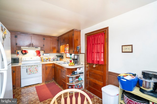 kitchen with white appliances, a sink, light countertops, under cabinet range hood, and wainscoting