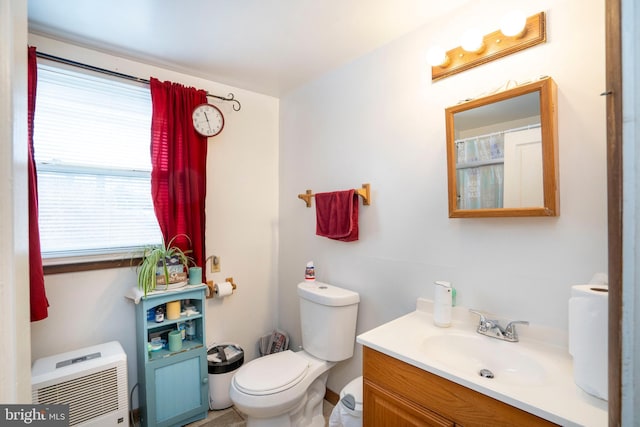 bathroom with heating unit, toilet, and vanity