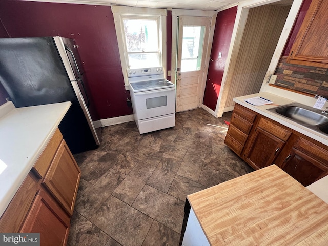 kitchen featuring light countertops, brown cabinets, freestanding refrigerator, white electric range, and a sink