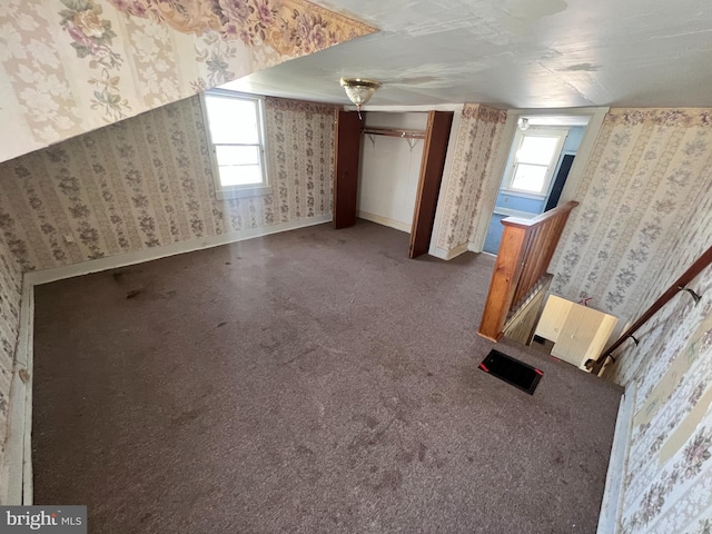 additional living space with wallpapered walls, baseboards, and dark carpet