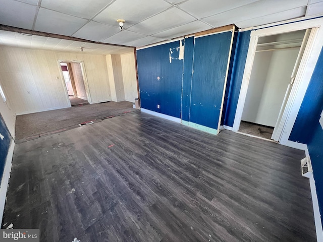 interior space featuring a drop ceiling, wood walls, baseboards, and wood finished floors