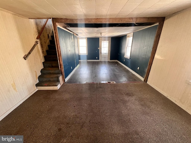 carpeted entrance foyer with stairway, baseboards, and wood walls