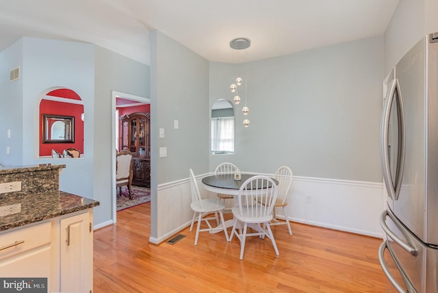 dining room featuring light wood-style flooring, arched walkways, visible vents, and baseboards