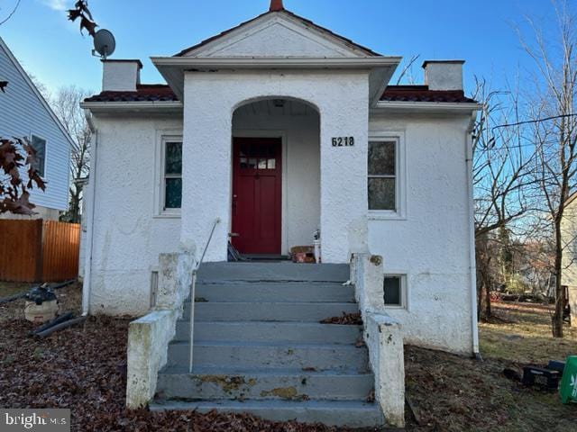 view of front of house with stucco siding, fence, and a chimney