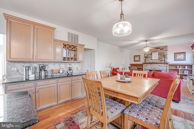 dining room featuring a fireplace, light wood-style floors, visible vents, and ceiling fan