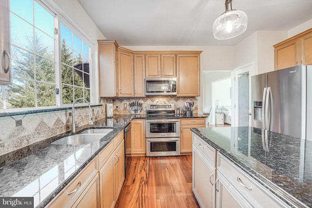 kitchen featuring light wood-style flooring, a sink, dark stone countertops, tasteful backsplash, and stainless steel appliances