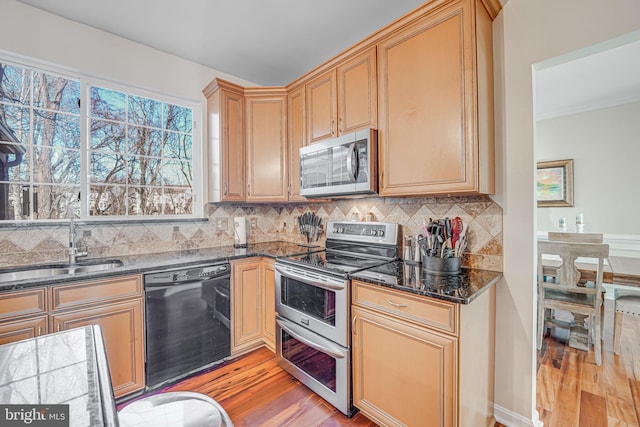 kitchen featuring dark stone counters, a sink, light wood-style floors, appliances with stainless steel finishes, and tasteful backsplash