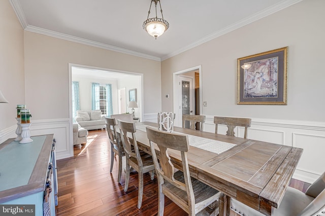 dining space featuring dark wood finished floors, a decorative wall, wainscoting, and ornamental molding