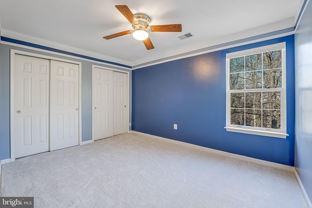 unfurnished bedroom with baseboards, carpet, visible vents, and multiple closets