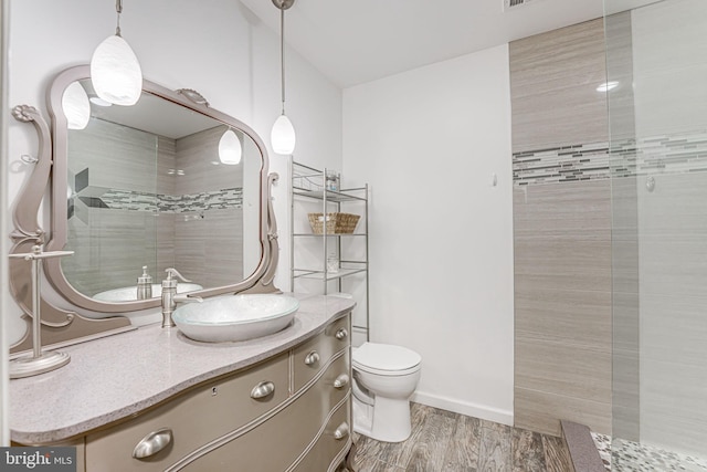 bathroom featuring baseboards, toilet, tiled shower, wood finished floors, and vanity