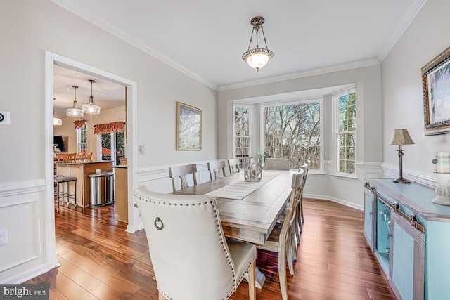 dining area with a decorative wall, wainscoting, ornamental molding, and wood-type flooring