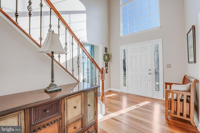 entryway featuring stairway, light wood-style flooring, a high ceiling, and baseboards