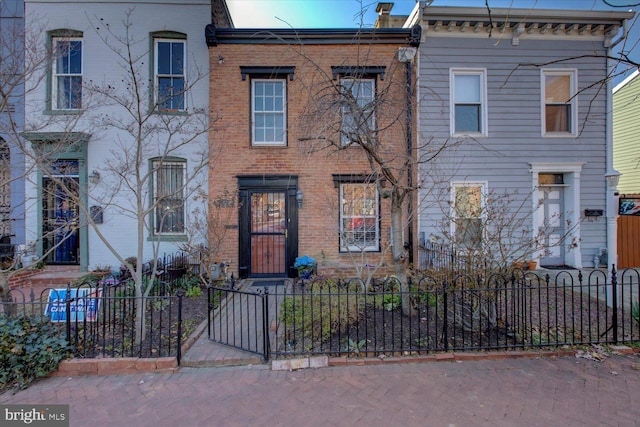 view of front of property featuring brick siding, a fenced front yard, and a chimney