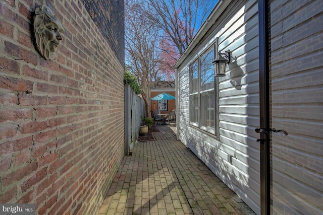 view of side of property with a patio, brick siding, and fence